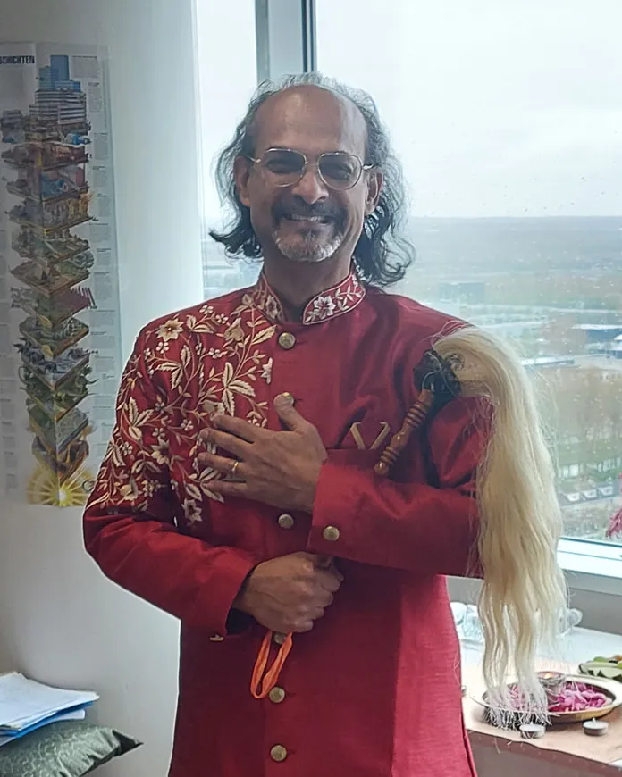 Portret van Aniel Ramjanam in een rode jas voor een raam met uitzicht.